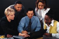 Five business people huddled around a laptop computer.